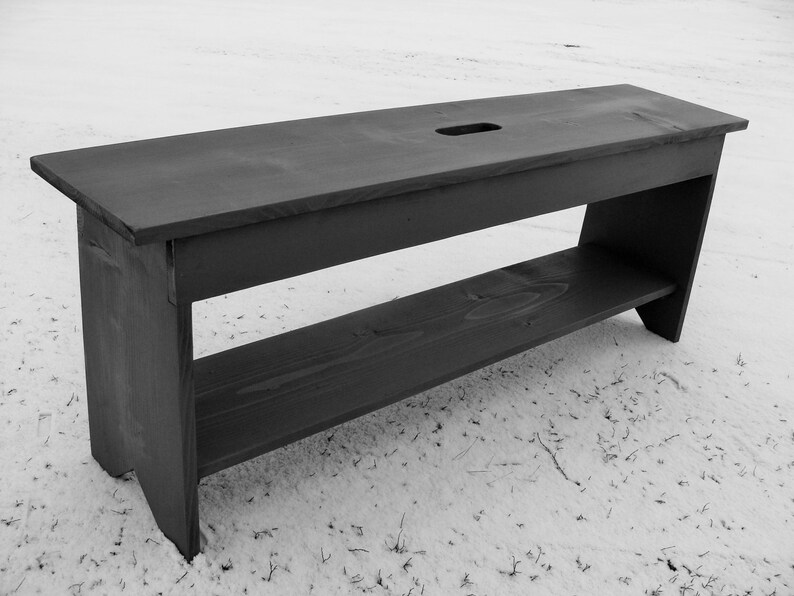 Pu&ograve; includere: Una panca in legno nero con uno scaffale. La panca ha un piano rettangolare con un piccolo foro al centro. Lo scaffale &egrave; sotto il piano ed &egrave; anch'esso in legno.