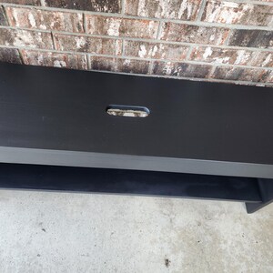 May include: Black wooden bench with a single shelf and a rectangular cutout in the top surface.