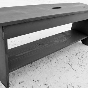 Pu&ograve; includere: Una panca in legno nero con uno scaffale. La panca &egrave; realizzata in legno grezzo e ha un design semplice.