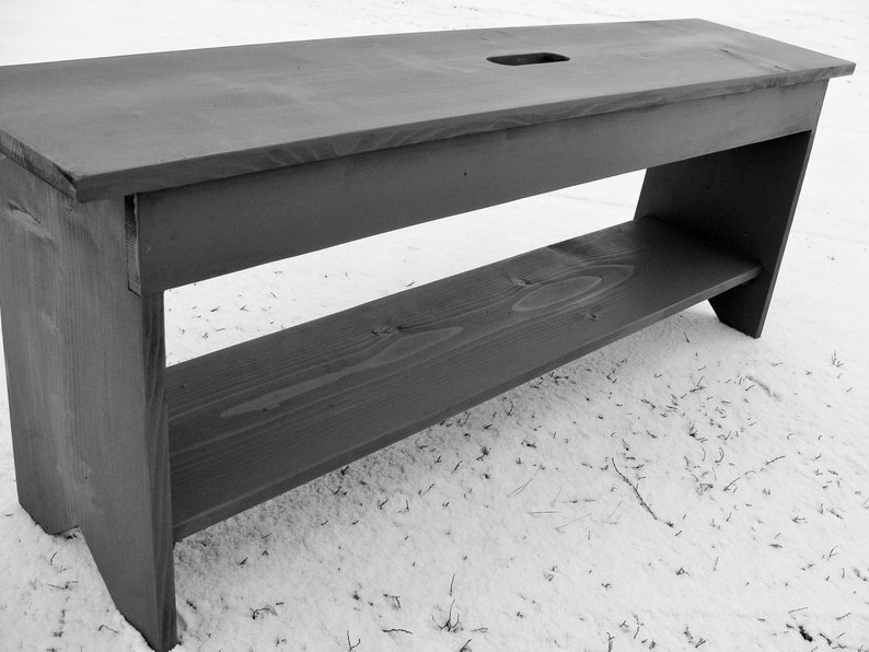 Pu&ograve; includere: Una panca in legno nero con uno scaffale. La panca &egrave; realizzata in legno grezzo e ha un design semplice.
