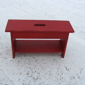 May include: A red wooden bench with a shelf. The bench has a cutout in the top.