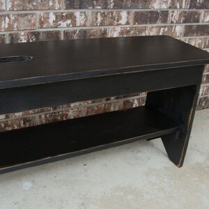 May include: Black wooden bench with a shelf underneath. The bench has a distressed finish and a small cutout in the top.