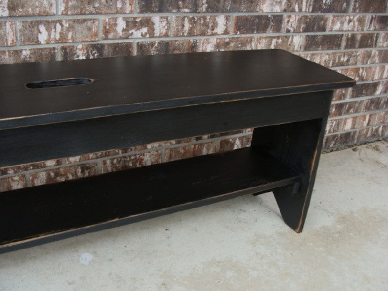 May include: Black wooden bench with a shelf underneath. The bench has a distressed finish and a small cutout in the top.
