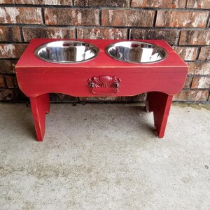 Puede incluir: Soporte de comida para perros de madera roja con dos cuencos de acero inoxidable. El soporte tiene una manija decorativa en la parte delantera.