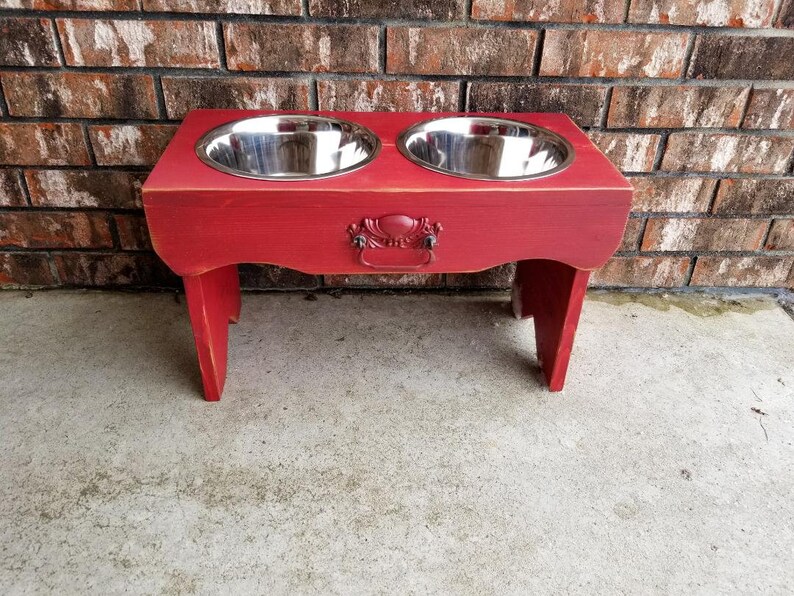 Puede incluir: Soporte de comida para perros de madera roja con dos cuencos de acero inoxidable. El soporte tiene una manija decorativa en la parte delantera.