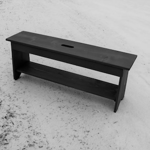 Pu&ograve; includere: Una panca di legno nera con uno scaffale sotto. La panca &egrave; su una superficie bianca.