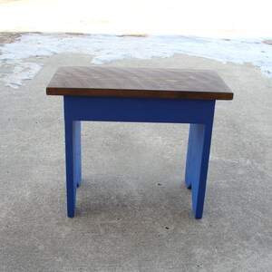 Puede incluir: Peque&ntilde;a mesa de madera con una tapa marr&oacute;n oscuro y patas azules vibrantes. La mesa mide aproximadamente 61 cm de largo, 30 cm de ancho y 46 cm de alto. El dise&ntilde;o es simple y r&uacute;stico, adecuado para varios usos.