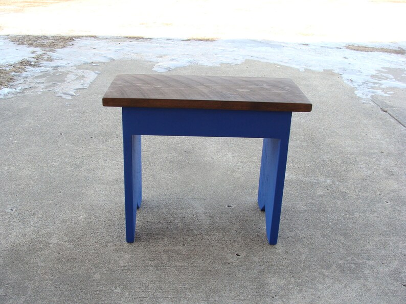 Puede incluir: Peque&ntilde;a mesa de madera con una tapa marr&oacute;n oscuro y patas azules vibrantes. La mesa mide aproximadamente 61 cm de largo, 30 cm de ancho y 46 cm de alto. El dise&ntilde;o es simple y r&uacute;stico, adecuado para varios usos.