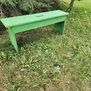 May include: A green wooden bench with a simple design, sitting on a grassy lawn.