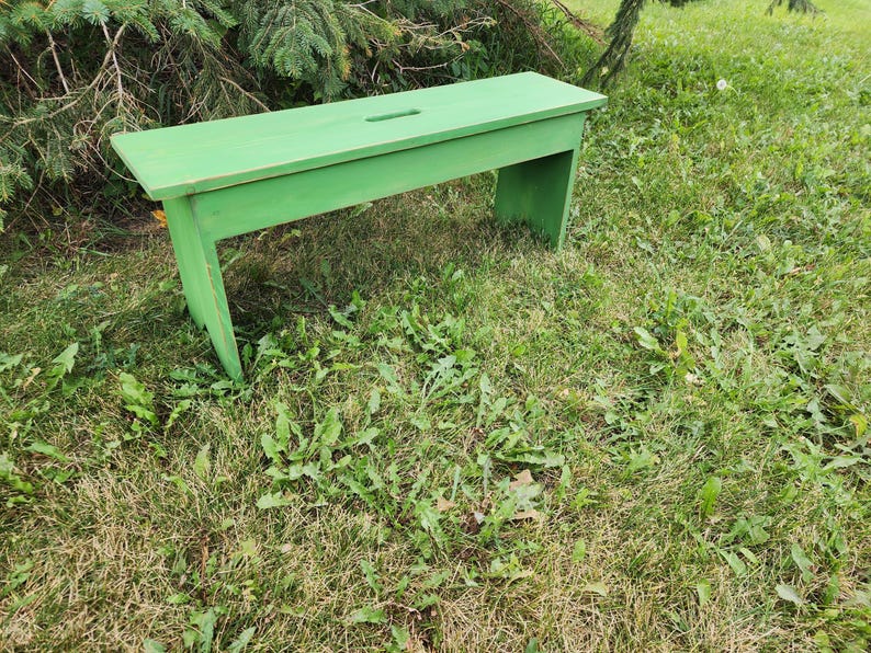 May include: A green wooden bench with a simple design, sitting on a grassy lawn.