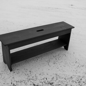 Pu&ograve; includere: Una panca in legno nero con uno scaffale e un piccolo foro nella parte superiore. La panca &egrave; seduta su una superficie innevata.