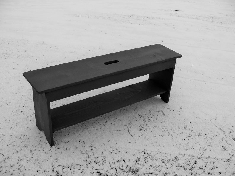 Pu&ograve; includere: Una panca in legno nero con uno scaffale e un piccolo foro nella parte superiore. La panca &egrave; seduta su una superficie innevata.