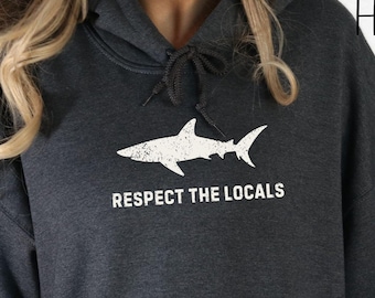 May include: Dark heather grey hoodie with a white shark silhouette and the text "Respect the Locals".