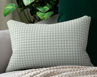May include: A rectangular pillow with a light green and white gingham pattern rests on a gray sofa, alongside a dark green pillow. A cream-colored knitted throw blanket is draped over the sofa. A large green plant is in the background.