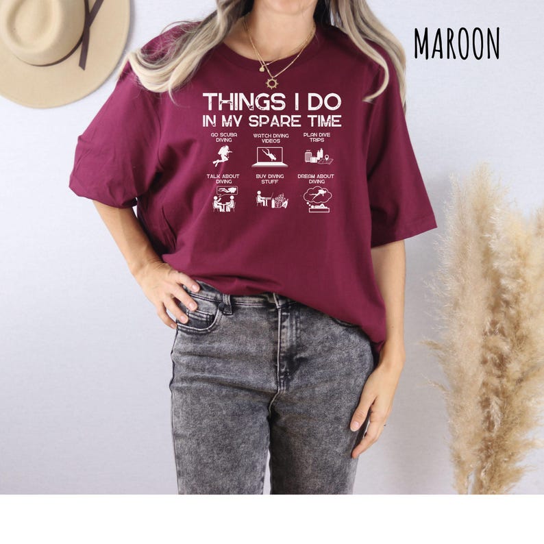 K&ouml;nnte beinhalten: Bordeauxfarbenes T-Shirt mit dem Text "THINGS I DO IN MY SPARE TIME" und Tauch-Symbolen. Das Shirt hat einen Rundhalsausschnitt und kurze &Auml;rmel. Das Wort "MAROON" ist oben rechts aufgedruckt.