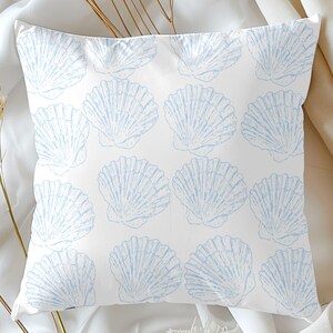 May include: Square white pillow with a repeating pattern of light blue seashell illustrations. The pillow is made of a soft fabric and is likely for decorative use. The design evokes a coastal or beach theme.