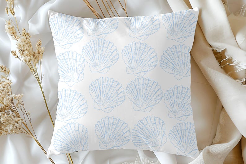 May include: Square white pillow with a repeating pattern of light blue seashell illustrations. The pillow is made of a soft fabric and is likely for decorative use. The design evokes a coastal or beach theme.