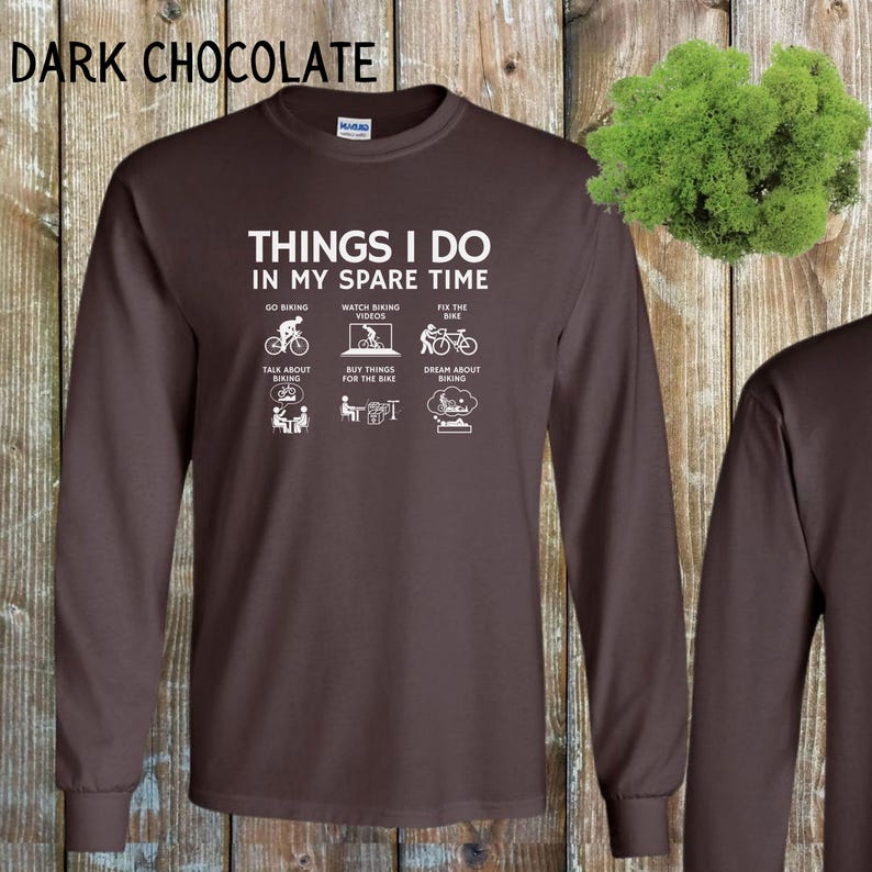 May include: A dark brown long-sleeve t-shirt with white text that reads "Things I do in my spare time" and features six icons depicting activities related to cycling. The icons include going biking, watching biking videos, fixing the bike, talking about biking, buying things for the bike, and dreaming about biking.