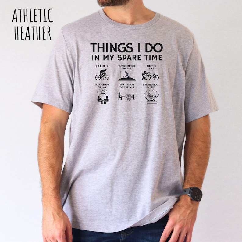 May include: A heather grey t-shirt with the text "Things I do in my spare time" and a series of icons depicting activities related to cycling. The icons include going biking, watching biking videos, fixing a bike, talking about biking, buying things for the bike, and dreaming about biking.