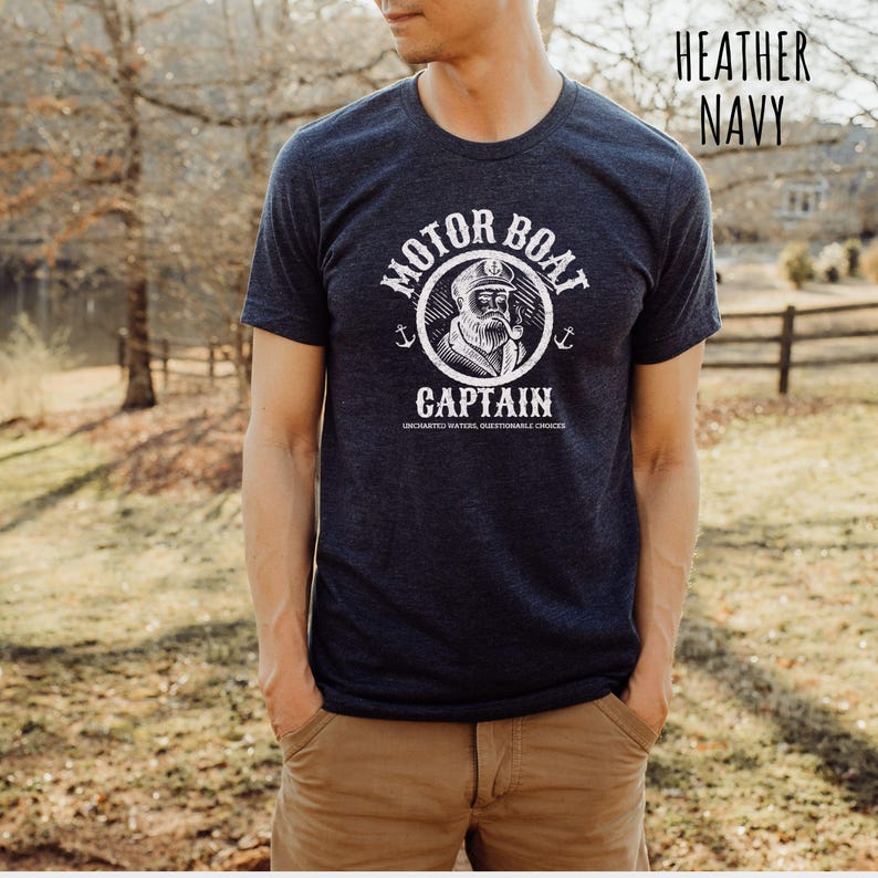 May include: A heather navy blue t-shirt with a white graphic of a sailor with a pipe and the text "Motor Boat Captain Uncharted Waters Questionable Choices".