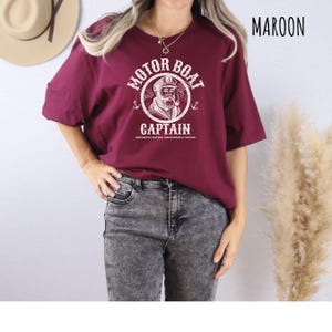 May include: A maroon t-shirt with a white graphic of a cartoon sailor with a beard and the text "Motor Boat Captain Uncharted Waters Questionable Choices".