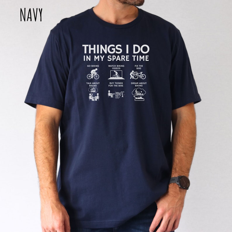 May include: A navy blue t-shirt with a white graphic that says "Things I do in my spare time" and shows icons of a person cycling, watching cycling videos, fixing a bike, talking about cycling, buying things for the bike, and dreaming about cycling.