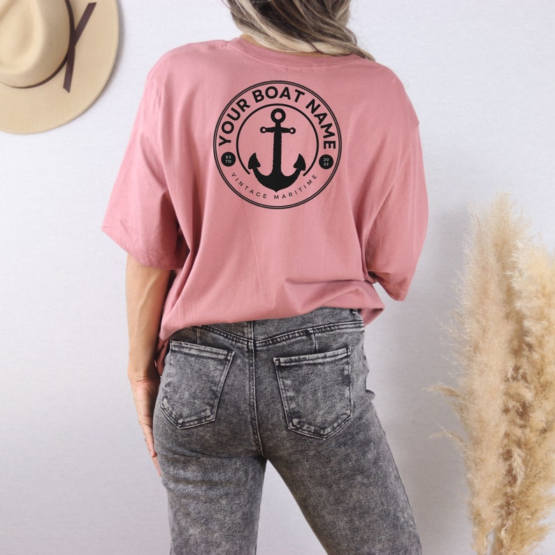 May include: A pink t-shirt with a black anchor graphic and the text "YOUR BOAT NAME" in a circle. The text "VINTAGE MARITIME" is also in the circle.