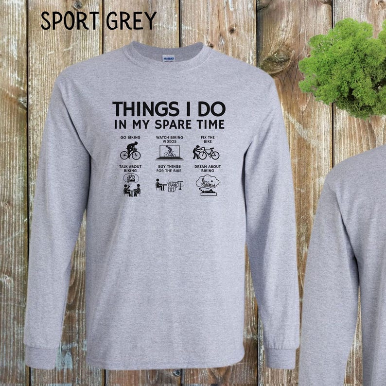 May include: A gray long-sleeve t-shirt with the text "Things I do in my spare time" and illustrations of people biking. The text below the illustrations includes "Go Biking", "Watch Biking Videos", "Fix the Bike", "Talk About Biking", "Buy Things for the Bike", and "Dream About Biking".
