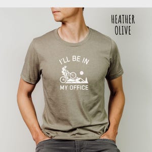 May include: A heather olive t-shirt with a white graphic of a person riding a mountain bike with the text "I'll be in my office".