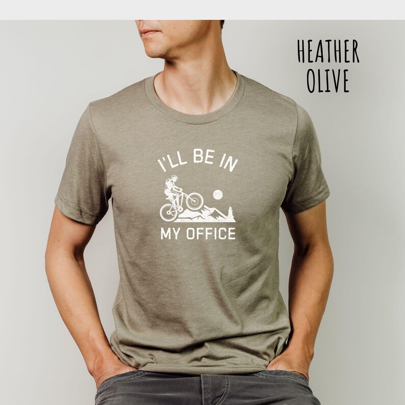 May include: A heather olive t-shirt with a white graphic of a person riding a mountain bike with the text "I'll be in my office".