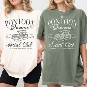 Pu&ograve; includere: Due t-shirt da donna in avorio e verde muschio con un design grafico di una barca ponton e il testo "Pontoon Queens Social Club Est. 2024 Keep Calm and Pontoon On."