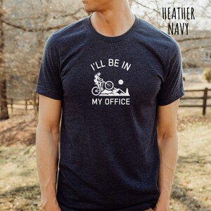 May include: A heather navy t-shirt with a white graphic of a person riding a mountain bike up a hill with the text "I'll be in my office".