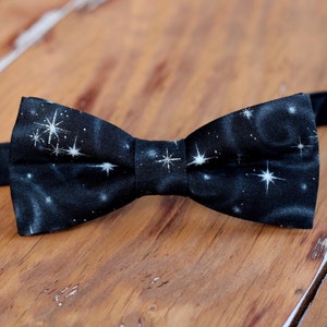 May include: A black bow tie with a white galaxy print. The bow tie is made of a soft, comfortable fabric and has a classic bow tie shape.
