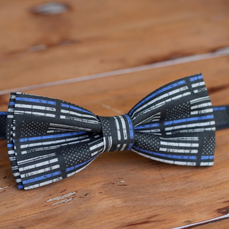 May include: A black bow tie with a thin blue and white striped pattern. The pattern resembles the thin blue line flag.