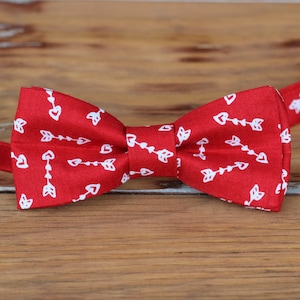 May include: Red bow tie with a white arrow and heart pattern.
