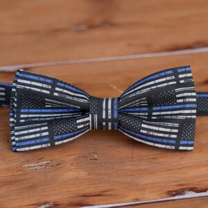 May include: A black bow tie with a thin blue and white striped pattern. The pattern resembles the American flag with a thin blue line added to represent law enforcement.