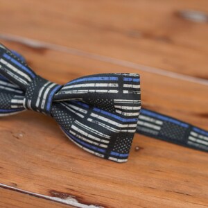 May include: A black bow tie with a thin blue and white striped pattern. The pattern resembles a thin blue line flag.