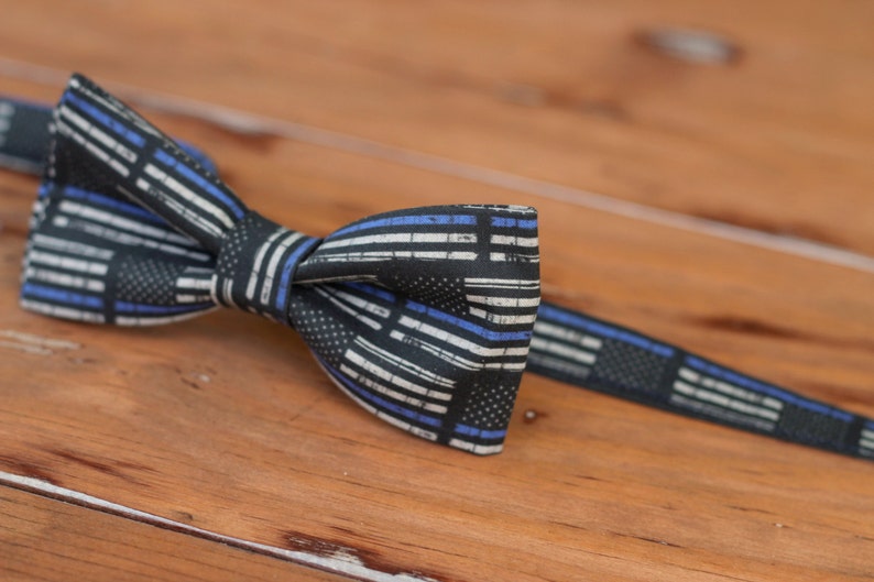 May include: A black bow tie with a thin blue and white striped pattern. The pattern resembles a thin blue line flag.