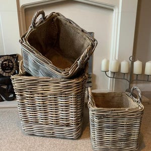 May include: Three woven wicker baskets with natural jute lining. The baskets are stacked on top of each other, with the largest basket at the bottom and the smallest basket at the top. The baskets are a light grey colour with a natural woven pattern.