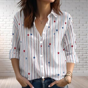 May include: White button-down shirt with vertical red and blue stripes and scattered red and blue stars. The shirt has long sleeves that are rolled up to the elbows. The shirt is unbuttoned at the top.