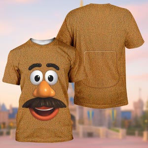 Può includere: Una maglietta marrone con un design a volto di cartone animato, che include grandi occhi, un naso e un baffo. La maglietta ha un aspetto strutturato e un dettaglio di tasca sul retro. Il design è di un personaggio divertente e stravagante.
