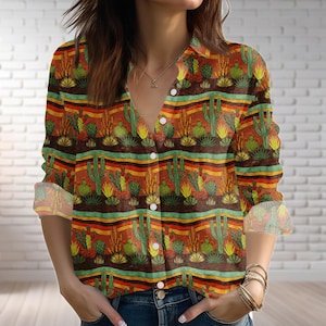 Peut inclure: Une chemise boutonnée avec un motif de cactus du désert. La chemise a un col en V et des manches longues. Le motif comprend des cactus, des plantes succulentes et des rayures horizontales marron, vert, jaune et rouge.