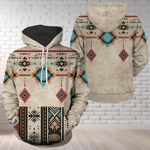 Op de afbeelding: Een beige hoodie met een zwart gevoerde capuchon en een op het zuidwesten geïnspireerd patroon. Het ontwerp bevat geometrische vormen in teal, rood, bruin en zwart. De voor- en achterkant van de hoodie tonen hetzelfde patroon.