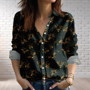 May include: Dark green button-down shirt with a repeating pattern of gold and black bees. The long-sleeved shirt has a collared neckline and white buttons. The sleeves are rolled up, revealing a lighter green fabric. The shirt is made of a soft, comfortable material.