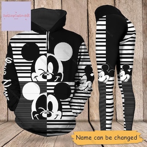 Puede incluir: Sudadera y leggings a rayas blancas y negras con un diseño de Mickey Mouse. La sudadera tiene una gran cabeza de Mickey Mouse en la parte delantera y los leggings tienen una cabeza de Mickey Mouse más pequeña en cada pierna. El texto "Your Name" está impreso en la sudadera.