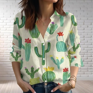 May include: A button-down shirt with a cactus print. The shirt features a light beige background with watercolor illustrations of various cacti in shades of green, with red, yellow, and purple flowers. The long-sleeved shirt has a collared neckline.