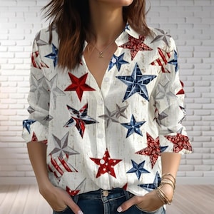 May include: White button-down shirt with a pattern of red, white, and blue stars. The long-sleeved shirt has a V-neck and is made of a lightweight fabric. The stars vary in design, some with stripes and floral patterns.