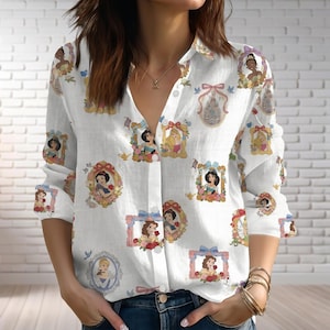 Könnte beinhalten: Weißes Button-Down-Shirt mit gerahmten Porträts von Disney-Prinzessinnen. Das langärmlige Hemd hat einen Kragen und ist mit verschiedenen Prinzessinnen-Illustrationen in verzierten Rahmen mit Schloss- und Schleifenakzenten verziert.