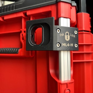 May include: A red and black storage container with a black Pak Lock ML4-H bracket. The bracket, secured with screws, features the Pak Lock logo. The container has a handle and is made of plastic. The image shows a close-up view.