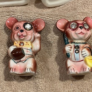 May include: Two ceramic mouse figurines with pink and brown coloring. One mouse holds a football and the other holds a golf club and a yellow bag. Both mice have rhinestone accents and are wearing outfits.
